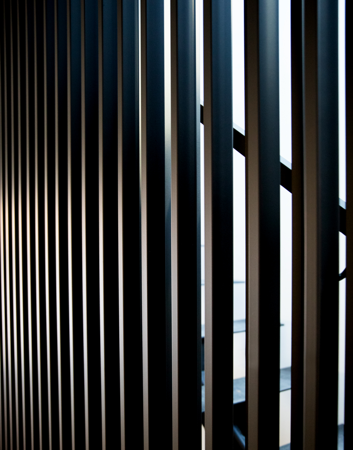 Long corridor view of vertical iron bars reflecting natural light, revealing sculptural detail and minimalist design.